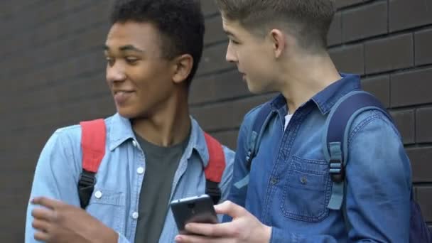 Többnemzetiségű tizenéves görgetés telefon és nevetve tiltott tartalom ellenőrzés hiánya — Stock videók