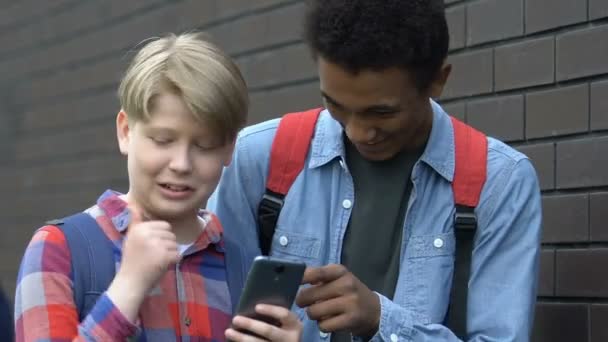 Tiszteletlen multifaji srácok görgetés okostelefon és nevetve, gúnyos — Stock videók
