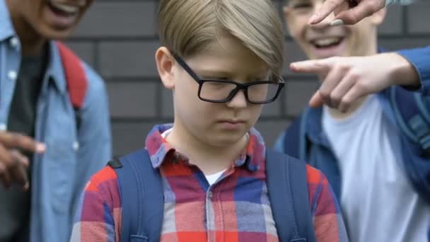 Studentengruppe zeigt mit dem Finger auf Jungen mit Brille, Außenstehender demütigt — Stockvideo