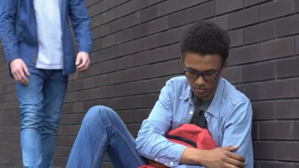 Дружелюбный студент протягивает руку афро-американскому подростку, поддерживая жертву издевательств — стоковое видео
