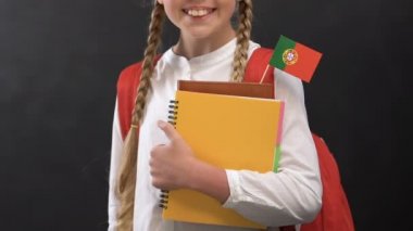 Portekiz bayrağı ile kitap tutan ve kameraya gülümseyen kız, dil eğitimi