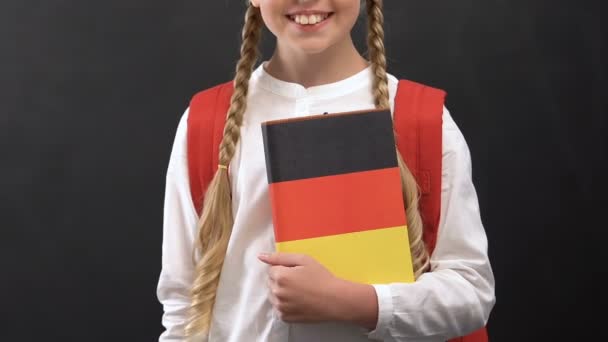 Симпатичная школьница с книжкой с немецким флагом, изучение языка, образование — стоковое видео