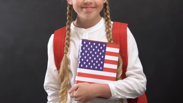 Colegiala sonriente sosteniendo libro con la bandera de EE.UU., Inglés idioma estudiando — Vídeos de Stock
