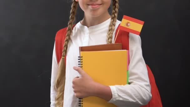 Маленька дівчинка тримає книги з іспанським прапором і посміхається на камеру, мова — стокове відео