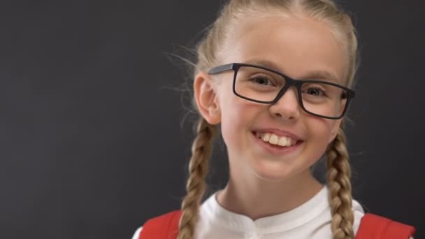 Feliz colegiala en anteojos sonriendo a la cámara contra pizarra, educación — Vídeo de stock