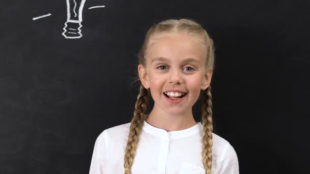 Niña inspirada apuntando con el dedo hacia la bombilla pintada en pizarra, creatividad — Vídeos de Stock