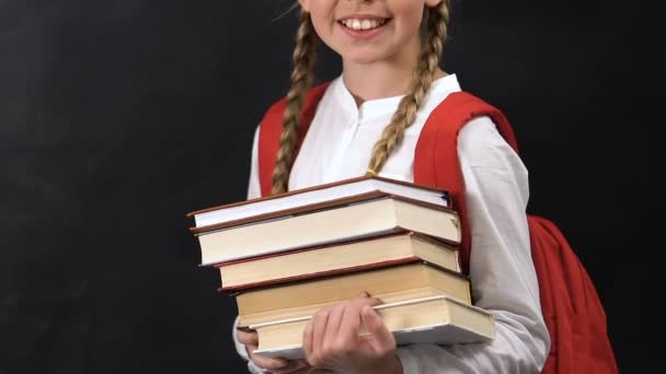 Alegre niña con mochila sosteniendo libros, disfrutando de las asignaturas escolares — Vídeo de stock