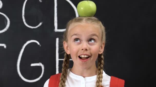 Rolig liten flicka som står med äpple på huvudet, alfabet skrivet på Blackboard — Stockvideo