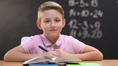 Matematik dersi sırasında okul masasında oturan ve kameraya bakan çocuk, eğitim