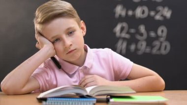 Matematik dersleri sırasında okul masasında oturan, kameraya bakan canı sıkılan küçük çocuk