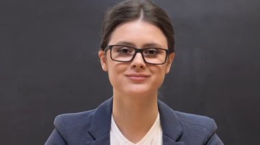 Kadın okul müdürü arka planda tahta karşı kamera bakıyor