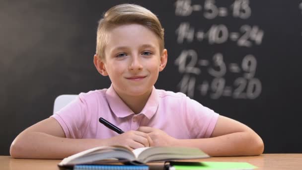 Αγόρι κάθεται στο σχολικό γραφείο κατά τη διάρκεια του μαθήματος μαθηματικά και κοιτάζοντας την κάμερα, εκπαίδευση — Αρχείο Βίντεο