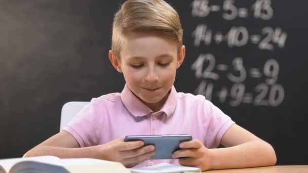 Pequeño niño jugando videojuego en el teléfono inteligente durante la lección de la escuela, mal alumno — Vídeos de Stock