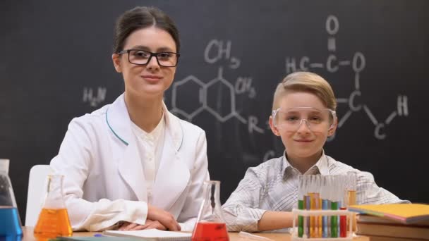 Petit garçon et professeur regardant dans la caméra à la leçon de chimie, laboratoire — Video