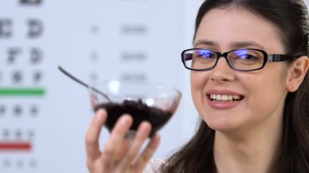 Menina sorridente em óculos mostrando mirtilo na câmera, prazer para a saúde dos olhos — Vídeo de Stock