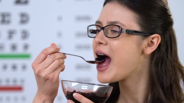 Happy female wearing eyeglasses eating bilberry, vitamins for healthy vision — Stock Video
