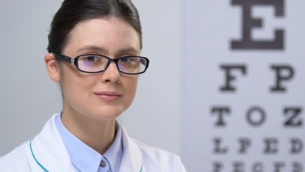 Профессиональная женщина-оптик смотрит в камеру на фоне диаграммы глаза — стоковое видео