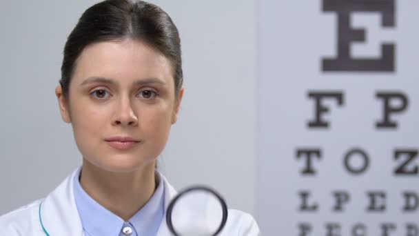 Улыбающаяся медсестра смотрит на камеру через увеличительное стекло, проверку здоровья, зрение — стоковое видео