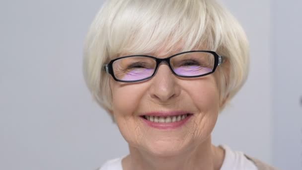 Mujer anciana sonriente con anteojos cerrando un ojo, revisando la visión en la clínica — Vídeo de stock