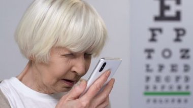 Görme sorunları olan yaşlı kadın akıllı telefonda mesaj okuma, körlük