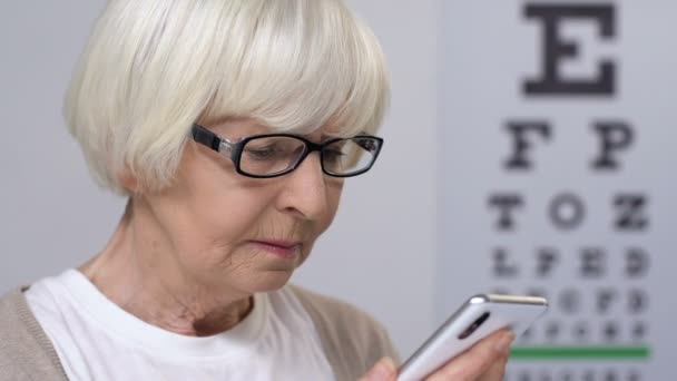 Ηλικίας γυναίκα σε γυαλιά διαβάζοντας μηνύματα στο smartphone, ασθένεια όραση — Αρχείο Βίντεο