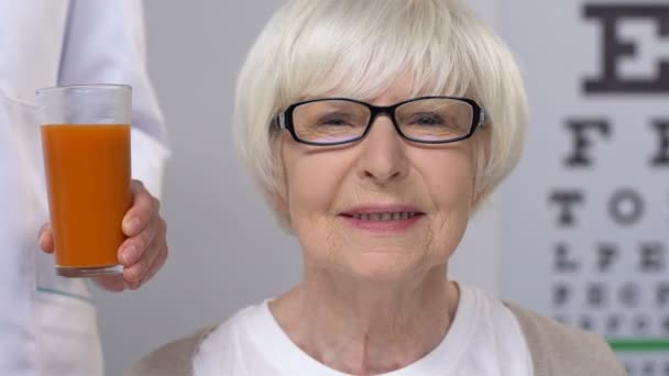 Doctor giving carrot juice to elderly female patient in eyeglasses, vitamins — Stock Video