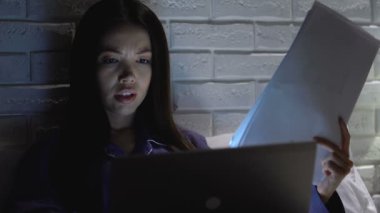 İş kadını uzaktan geceleri dizüstü bilgisayar üzerinde çalışıyor, belgelere bakıyor