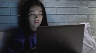 Yorgun kadın gece yatakta dizüstü bilgisayar kullanarak, uyku arzusu ile mücadele, iş