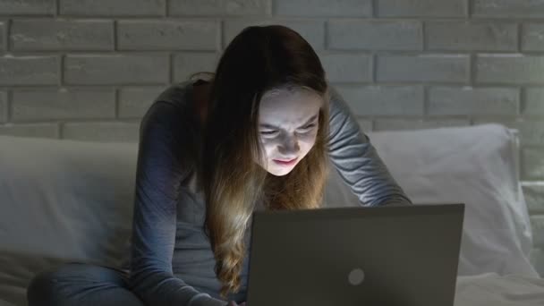 Женщина работает на ноутбуке в постели ночью, страдает от боли в шее, плохой осанки — стоковое видео