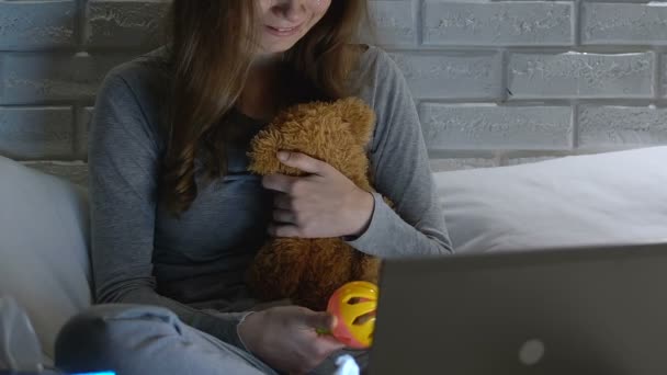 Mujer llorando sosteniendo el juguete del bebé y el oso de peluche delante de la computadora portátil, infertilidad — Vídeos de Stock