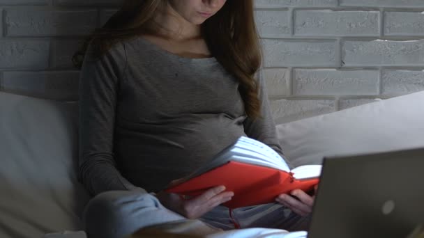 Femme enceinte lisant le livre et surfant sur Internet sur ordinateur portable la nuit, maternité — Video