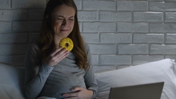 Llorando hembra embarazada comiendo donut delante de la computadora portátil, trastorno hormonal — Vídeo de stock