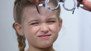 Optik deneme çerçevesi, göz muayenesi, miyopi giyen kadın çocuk gözlerini kısıyor