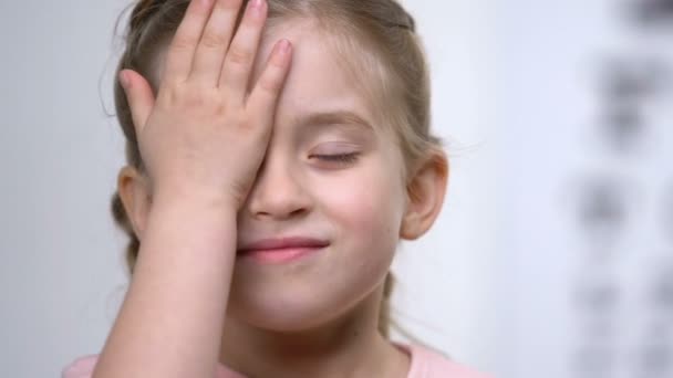 Schattig gelukkig schoolmeisje bedekt oog met de hand, medische consultatie oogheelkunde — Stockvideo