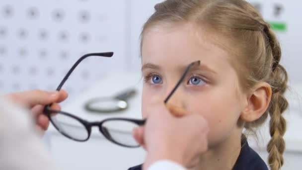 Θηλυκό οφθαλμίατρο επιλογή γυαλιά για χαμογελαστή μικρό κορίτσι, οπτικό πλαίσιο — Αρχείο Βίντεο