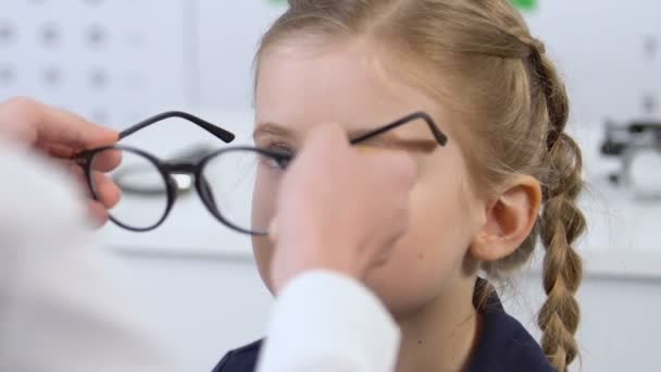 작은 소녀가 안경, 교정 렌즈를 착용하도록 돕는 안과 의사 — 비디오