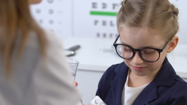 Niña pequeña en gafas tomando píldora con agua en el examen médico, tratamiento — Vídeos de Stock