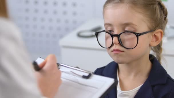 Niña mirando al optometrista llenando tarjeta de paciente, examen de vista — Vídeos de Stock