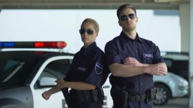 Cesur polis ve güneş gözlüğü adam arabanın yanında katlanmış elleri ile ayakta