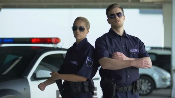 Brave politie vrouw en man in zonnebrillen staande met gevouwen handen in de buurt van auto — Stockvideo