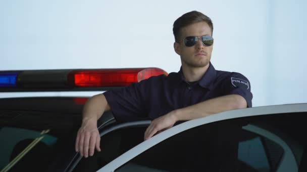 Friendly policeman in sunglasses standing near car and smiling, law and order — Stock Video