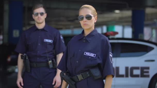 Серьезные женщина и мужчина полицейские в солнцезащитных очках стоять на открытом воздухе, безопасность — стоковое видео
