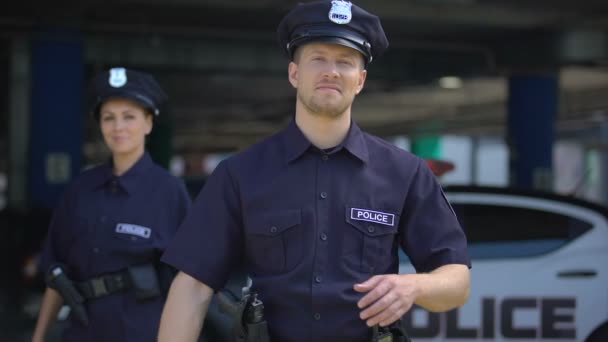 Amables agentes de policía sonriendo de pie cerca de la estación de policía, listos para ayudar, ordenar — Vídeo de stock