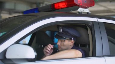 Arabada güneş gözlüğü takan ve kameraya gülümseyen genç polis, önemli bir iş