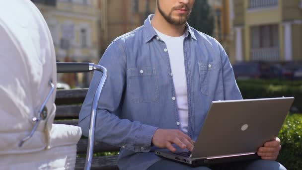 Giovane padre con passeggino che lavora al computer portatile nel parco cittadino, libero professionista — Video Stock