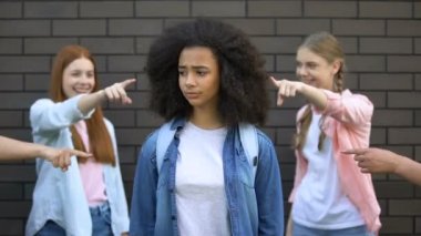 Aşağılanmış siyah kız öğrenci yüz elleri kapsayan, üniversite akranları parmakları işaret