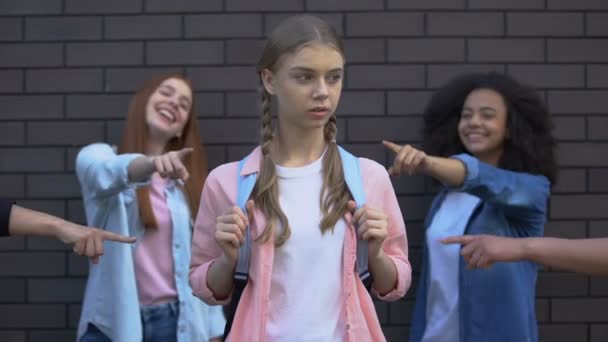 Compañeros de clase sonrientes señalando con los dedos a la pupila femenina con el bolso de la escuela, intimidación — Vídeos de Stock