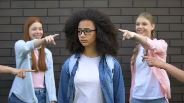 Hånfulla klasskamrater som pekar fingrar vid svart kvinnlig tonåring i glasögon — Stockvideo