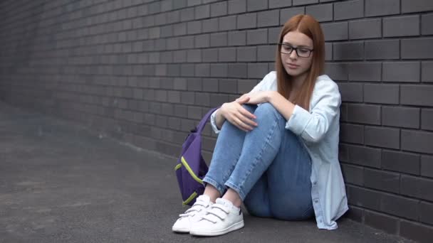 Eenzame vrouwelijke student brillen zittend vloer in middelbare school achtertuin, probleem — Stockvideo