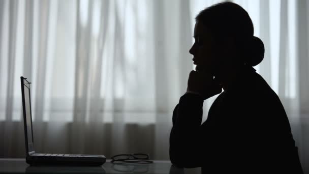 Silhouette einer Frau, die die Hände faltet und auf den Bildschirm ihres Laptops blickt und denkt — Stockvideo